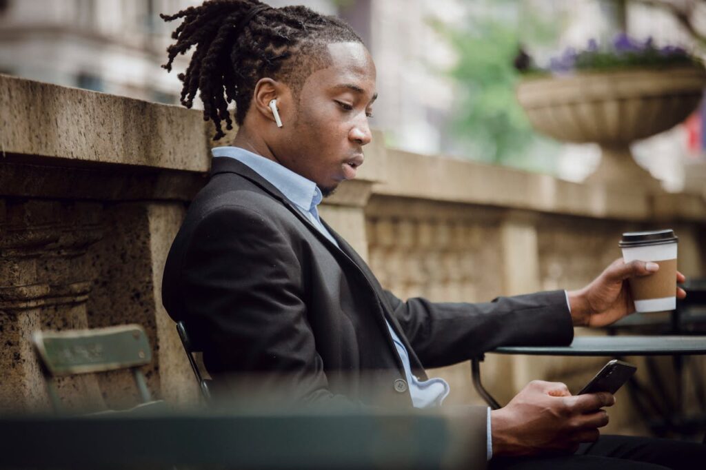 Serious black male messaging on smartphone while drinking coffee in outdoor cafe